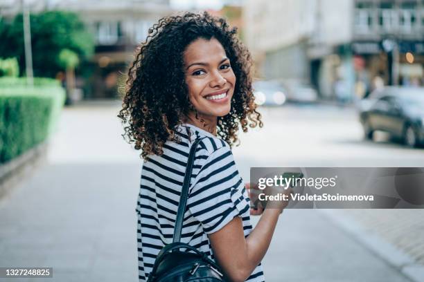 giovane donna sorridente che usa lo smartphone per strada. - guardare indietro foto e immagini stock
