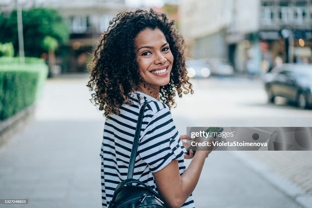 Young smiling woman using smartphone on the street.