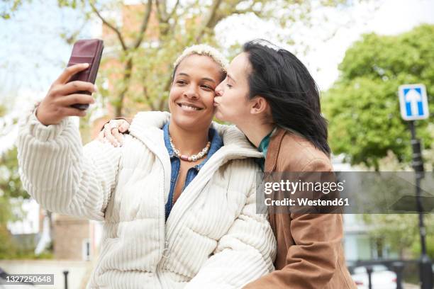 smiling woman taking selfie with girlfriend kissing on cheek - photos of lesbians kissing stock pictures, royalty-free photos & images