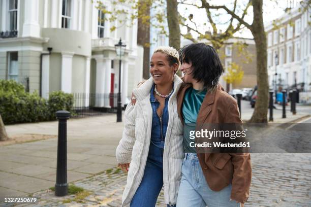 happy lesbian couple walking with arm around on footpath - couple london stockfoto's en -beelden