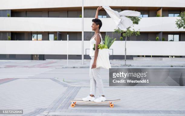businesswoman holding blazer while skateboarding with bag of vegetables on footpath - madrid shopping stock pictures, royalty-free photos & images