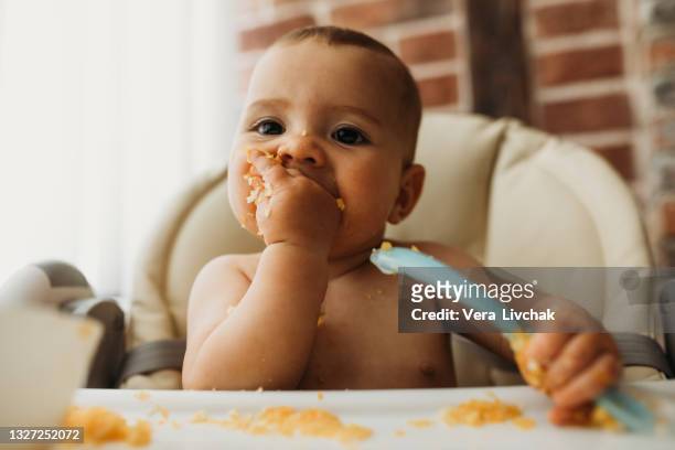 funny baby eating healthy food on kitchen - baby food fotografías e imágenes de stock