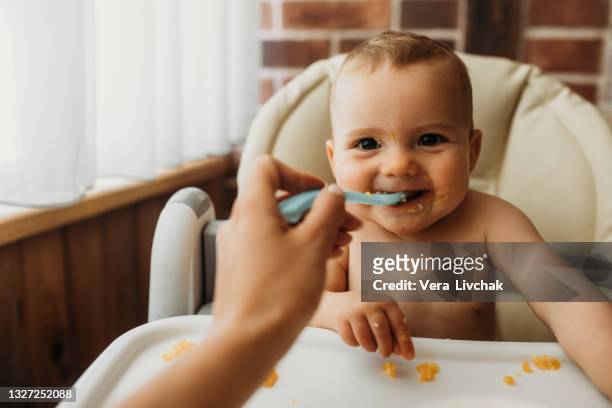 cute baby eating solid food from a spoon - babymat bildbanksfoton och bilder