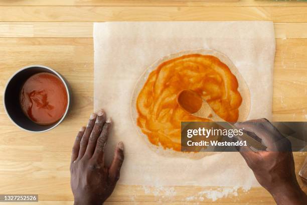 man spreading sauce while making pizza in kitchen - wachspapiere stock-fotos und bilder