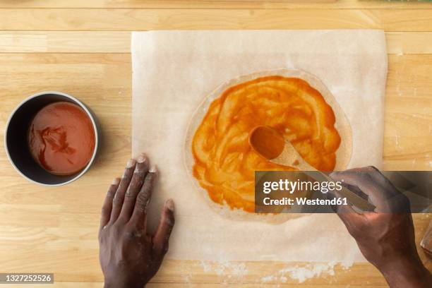 man spreading sauce while making pizza in kitchen - ワックスペーパー ストックフォトと画像