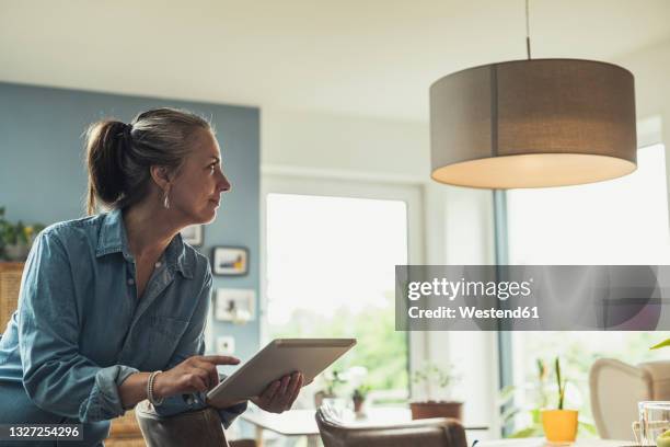 mature woman turning on lighting equipment with digital tablet at home - smart house stock pictures, royalty-free photos & images