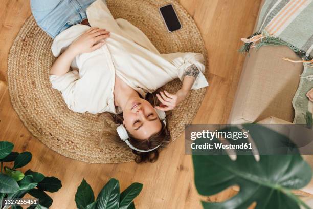 woman with eyes closed listening music while lying on floor at home - ropa tirada en el suelo fotografías e imágenes de stock