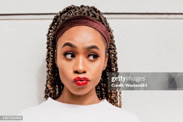 beautiful woman looking away with raised eyebrow in front of white wall - headband stock-fotos und bilder