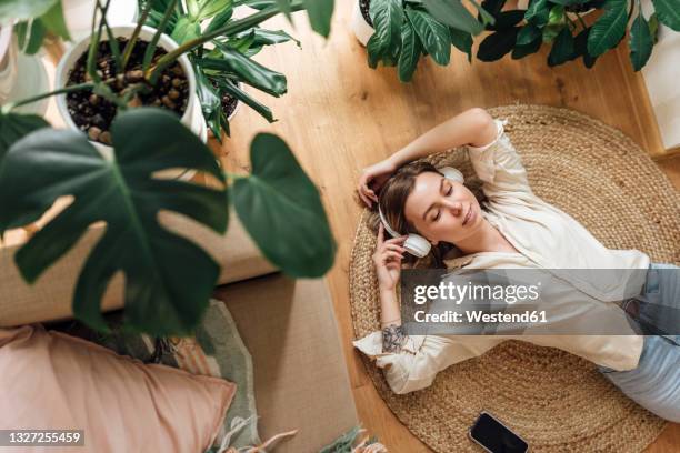 woman with hands raised listening music while relaxing on rug at home - holzboden von oben stock-fotos und bilder