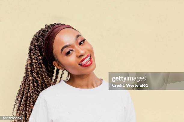 beautiful woman with head cocked sticking out tongue in front of yellow wall - tête penchée photos et images de collection