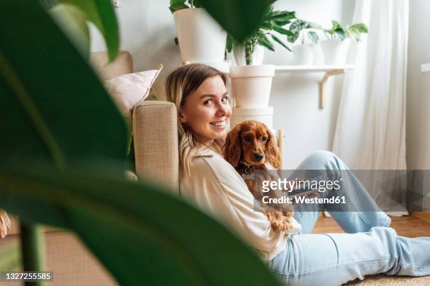 smiling young woman with dog holding smart phone at home - plant cell stockfoto's en -beelden
