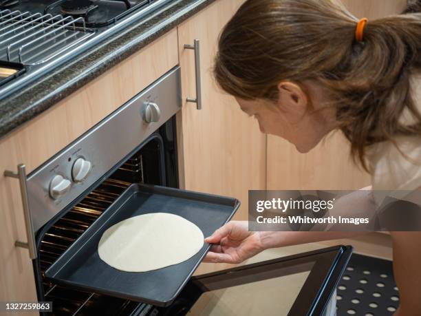 woman placing a tray of unleavened bread (matzo) dough in to a home oven to bake - matse stockfoto's en -beelden