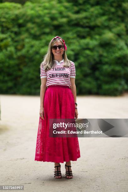 Guest wears a black and white print pattern scarf, black sunglasses, a red and white striped polo shirt with 'J'Adior California slogan, a black...