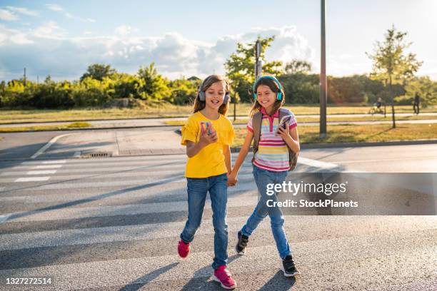 two girls are using phones and crossing the road - cross road children stock pictures, royalty-free photos & images