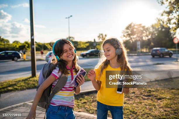 le bambine con le cuffie camminano e usano i loro telefoni - cartella scolastica foto e immagini stock