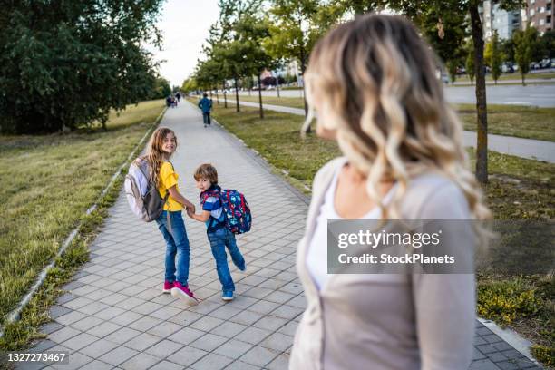 la madre single sta guardando i suoi figli andare da sola a scuola - famiglia con due figli foto e immagini stock