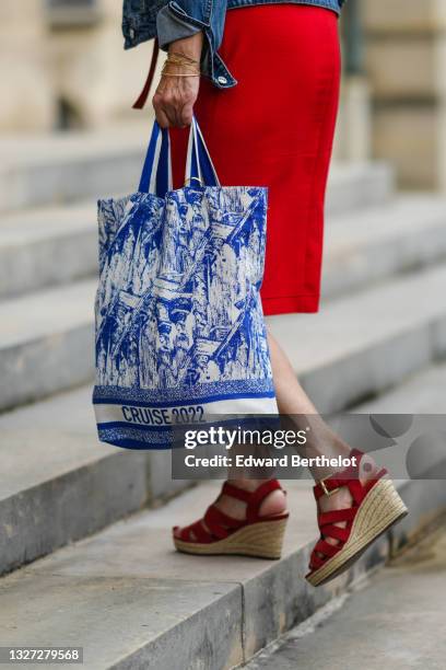 Guest wears a blue denim jacket, a red long dress, a blue and white print pattern Christian Dior tote-bag with Cruise 2022 slogan, red suede strappy...