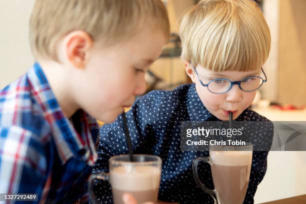 two young boys drink hot chocolate with straw - hot chocolate stock pictures, royalty-free photos & images