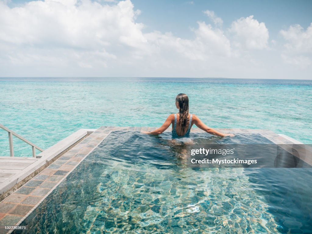 La mujer se relaja dentro de la piscina infinita sobre la laguna de arrecife