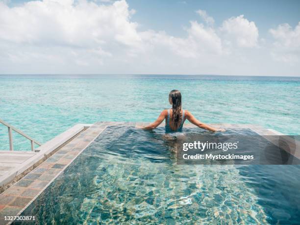 woman relaxes inside infinity pool over reef lagoon - maldivas imagens e fotografias de stock