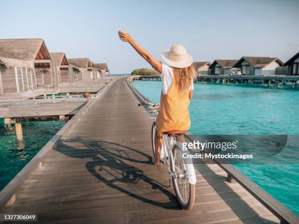 happy woman riding bicycle on wooden pier in the maldives - royalty free space images stockfoto's en -beelden