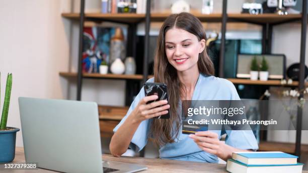 young woman paying online with credit card and lap top at home - phone credit card photos et images de collection
