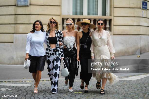 Gili Biegun wears black sunglasses, gold earrings, a white turtleneck puffy shoulder long sleeves shirt with embroidered, black shiny leather shorts,...