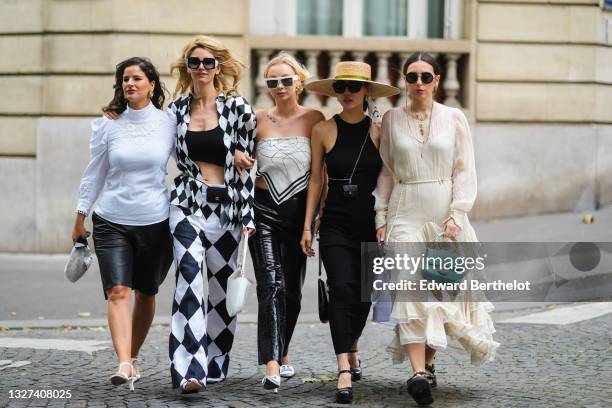 Gili Biegun wears black sunglasses, gold earrings, a white turtleneck puffy shoulder long sleeves shirt with embroidered, black shiny leather shorts,...