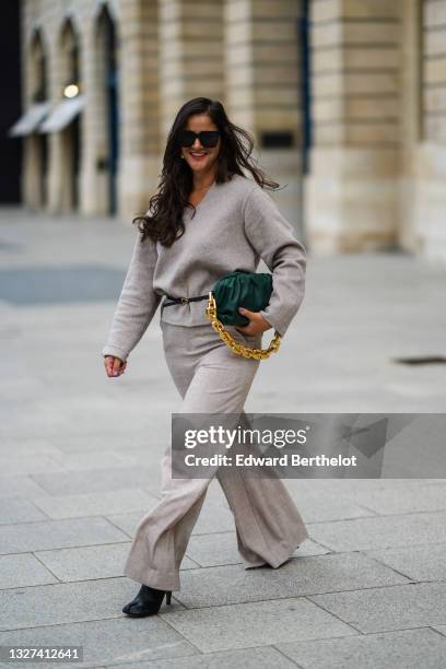 Gili Biegun wears black sunglasses, gold earrings, a gold chain necklace, a gray V-neck long sleeves pullover, matching gray large pants, a black...