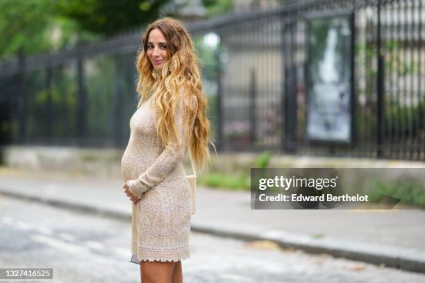 Guest wears a long embroidered print pattern tube dress with turtleneck and long sleeves, a beige shiny leather with pearls strap shoulder bag,...