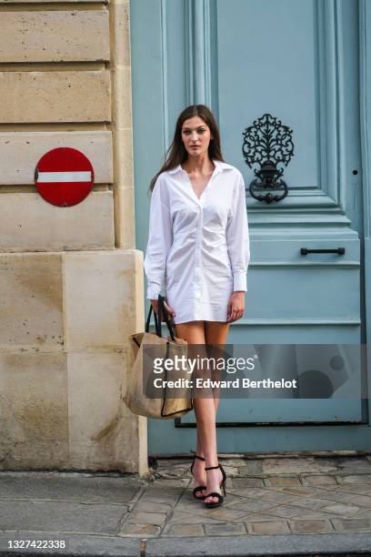 Model wears a white shirt short dress, a beige wicker handbag, black suede strappy pumps heels shoes / sandals, outside Armani, during Paris Fashion...