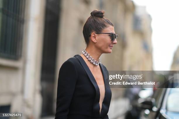Giovanna Battaglia wears black sunglasses, a silver large crystal necklace, a black long sleeves V-neck long dress, outside Armani, during Paris...