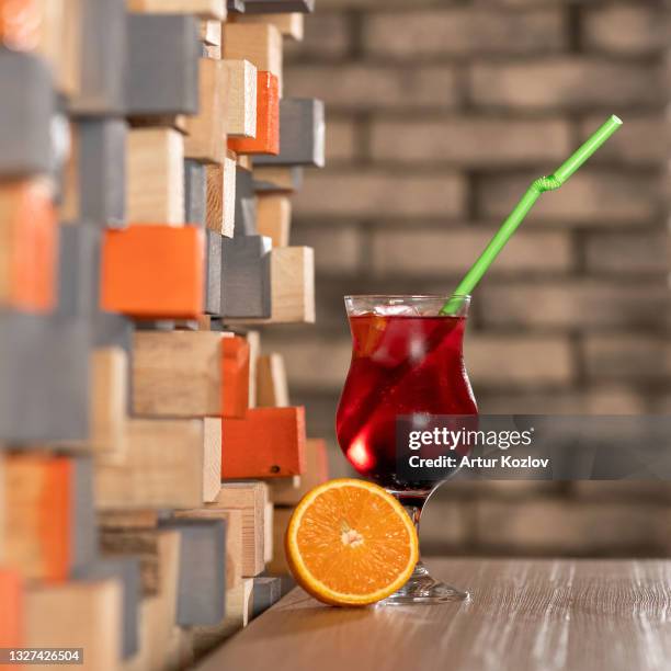 cold refreshing alcoholic drink. glass of red tropical beverage or cocktail on table with half of citrus on it. soft focus. copy space - glass half full party stock-fotos und bilder