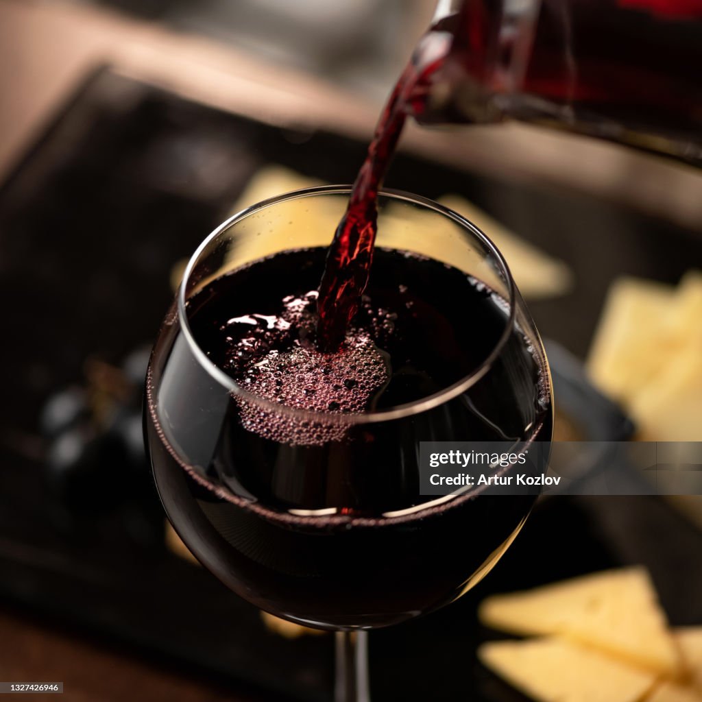 Expensive Red wine pouring into wine glass. Wineglass with merlot or sauvignon on Blurred background. Close up shot. Luxury Alcoholic drink or beverage