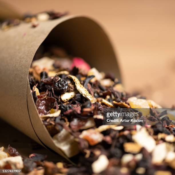 close up of dry herbal tea heap scattered from paper packaging on wooden background. fruit and berry tea with flower petals. soft focus - herbal tea bag stock pictures, royalty-free photos & images