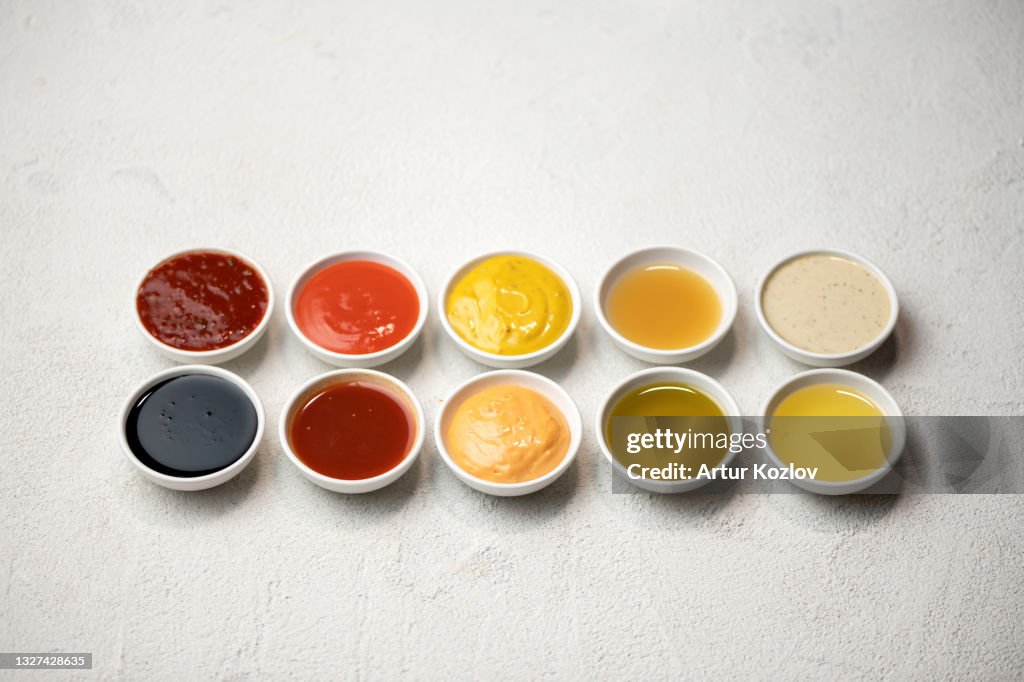 Big Set of colored sauces in Crockery. Different sauces, mayonnaise, mustard, soy sauce, oil and ketchup on white background. Top side view. Tasty food. Kitchen utensils
