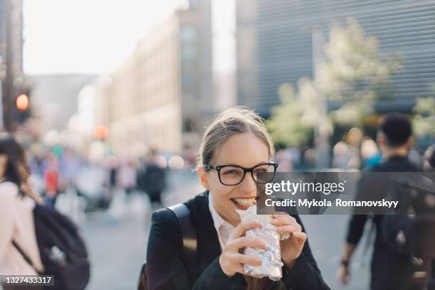 young business lady in glasses posing eating burrito on the busy street. - burrito stockfoto's en -beelden