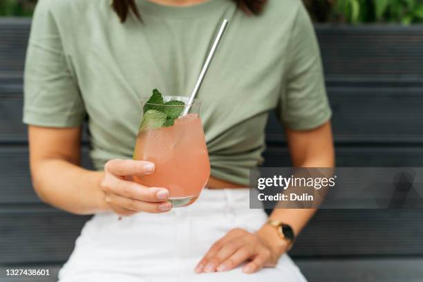 portrait of a woman with holding a paloma cocktail sitting on a bench - straw ストックフォトと画像