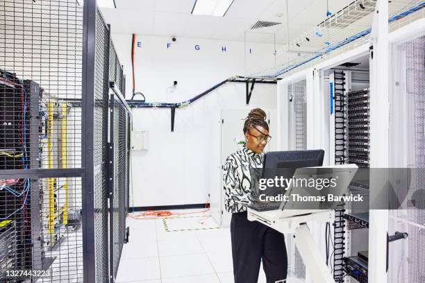 medium wide shot of female computer engineer configuring server in data center - computer server room stock pictures, royalty-free photos & images