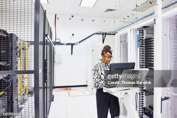 medium wide shot of female computer engineer configuring server in data center - sala de servidores - fotografias e filmes do acervo