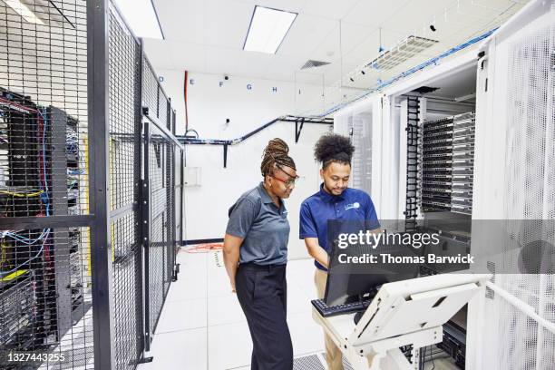 medium wide shot of it professionals in discussion while configuring server in data center - data center stockfoto's en -beelden