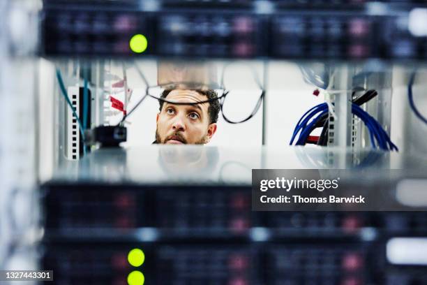 medium shot looking through server rack of male it professional working in data center - netwerkserver stockfoto's en -beelden
