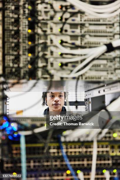 medium shot through server rack of female computer engineer working in data center - data center stockfoto's en -beelden