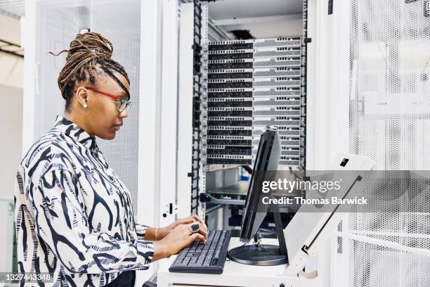 medium shot of female it professional configuring server in data center - native african ethnicity stock-fotos und bilder