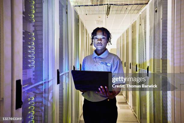medium shot portrait of female computer engineer holding laptop while working in row of servers in data center - it support server stock pictures, royalty-free photos & images