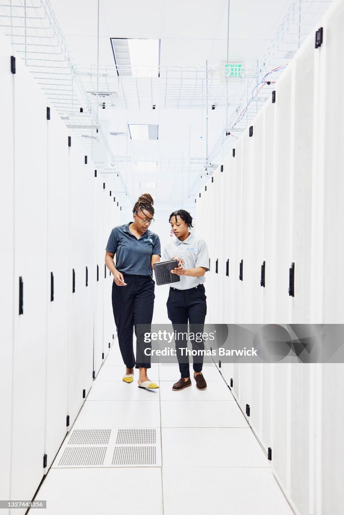 Wide shot of female IT professionals looking at data on digital tablet while working in data center