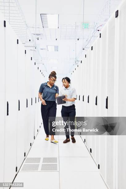 wide shot of female it professionals looking at data on digital tablet while working in data center - data centre stock pictures, royalty-free photos & images