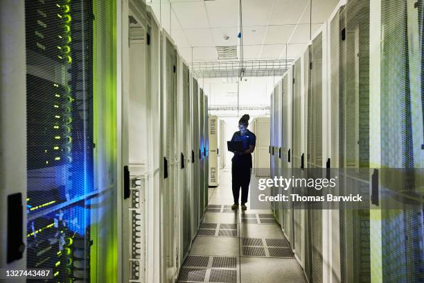 wide shot of female computer engineer using laptop while working in data centerr - native cloud services stock pictures, royalty-free photos & images