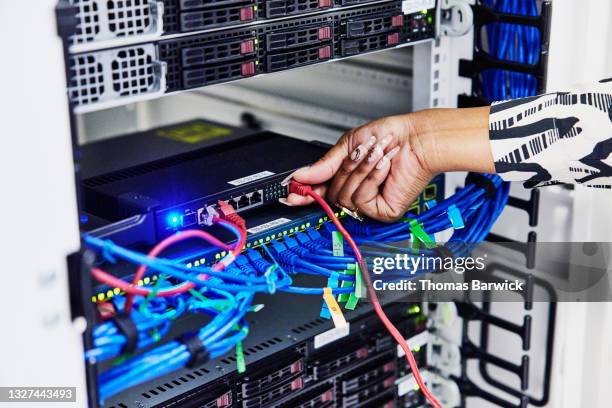 close up shot of female it professionals hand connecting ethernet cable to router in server rack while working in data center - co supported stock pictures, royalty-free photos & images