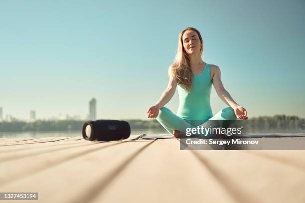 young woman practicing outdoor yoga at lake pier and listen music via bluetooth speaker - bluetooth photos et images de collection
